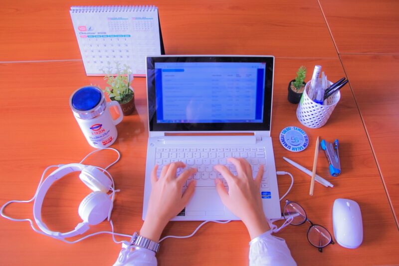 hands typing on computer with headphones and pencils in background, example of writing career 