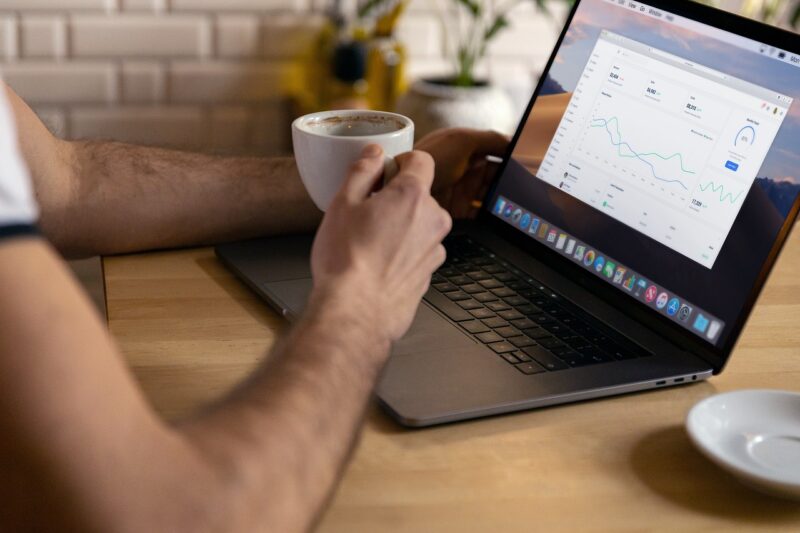 man sitting at table holding coffee with laptop open 