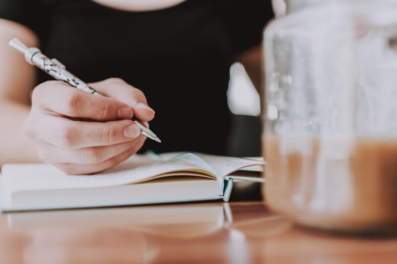 woman with pen in hand writing in notebook 