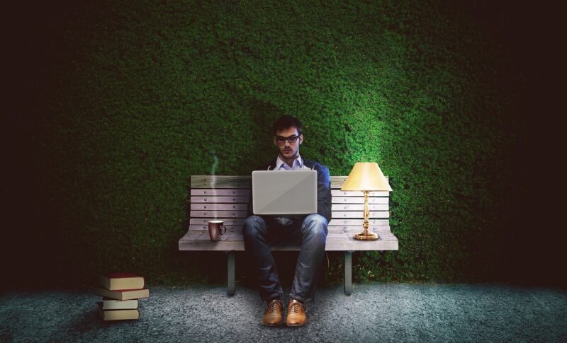 person sitting on bench with computer and books 