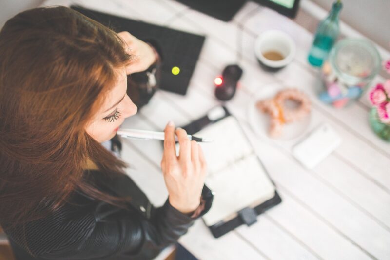 woman chewing on pen with notebook