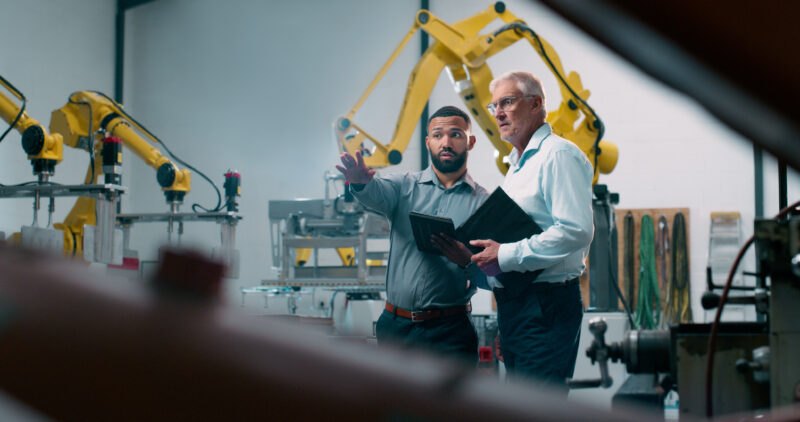 Robotics, people and engineer tablet with industrial collaboration and planning in warehouse. Factory, engineering and futuristic work of manufacturing management with discussion for cnc automation