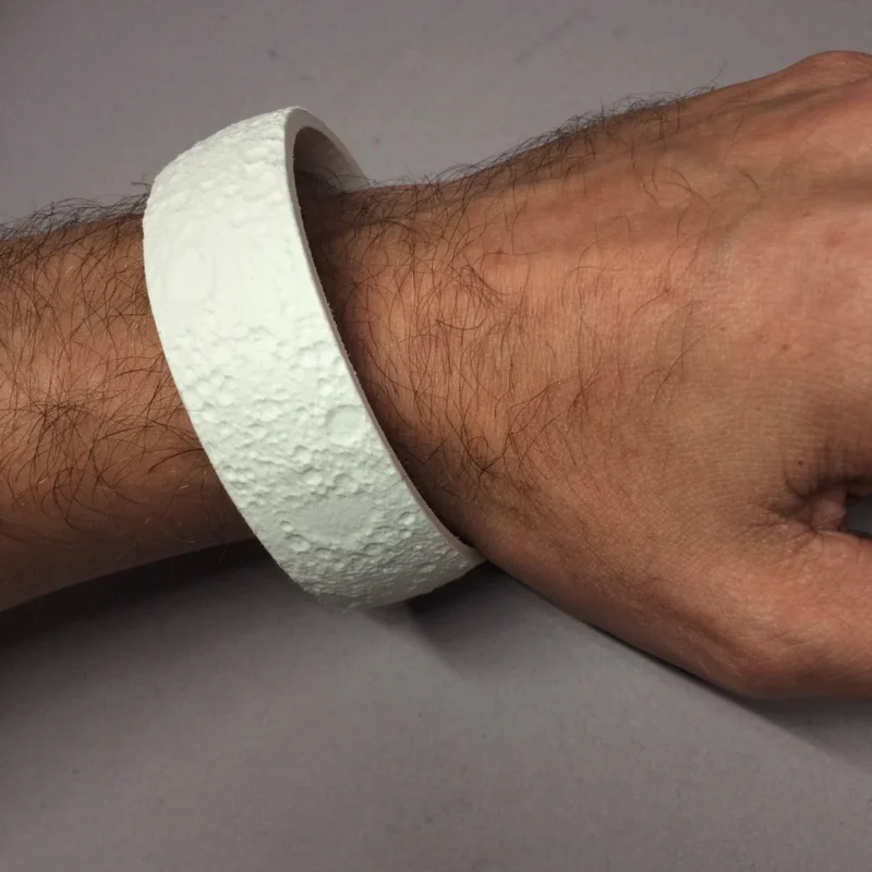 An arm wearing a bracelet that looks like the surface of the moon is shown.
