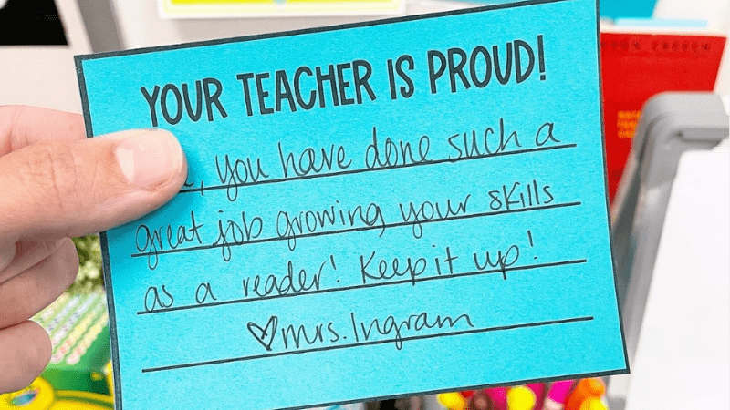 The Subtle Power of the Positive Note Home A hand holding a 'Your Teacher is Proud!' note on blue paper