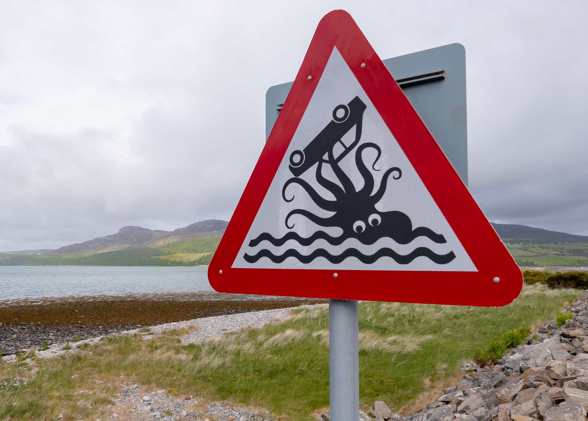 Picture Prompts: By the Sea A humorous road sign beside a causeway near the coastal village of Tongue in the northwest of Scotland. The warning sign notifies drivers that they are going to be driving close to the sea. The black and white illustration is of an octopus holding an upturned car in its tentacles.