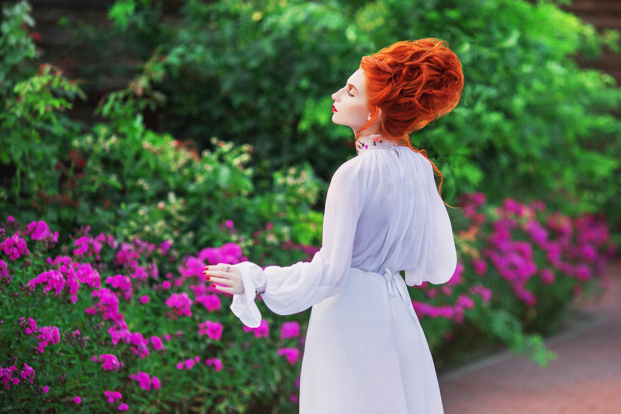 Picture Prompts: In the Garden A red-haired woman in an old-fashioned white dress stands in a garden, looking into the distance
