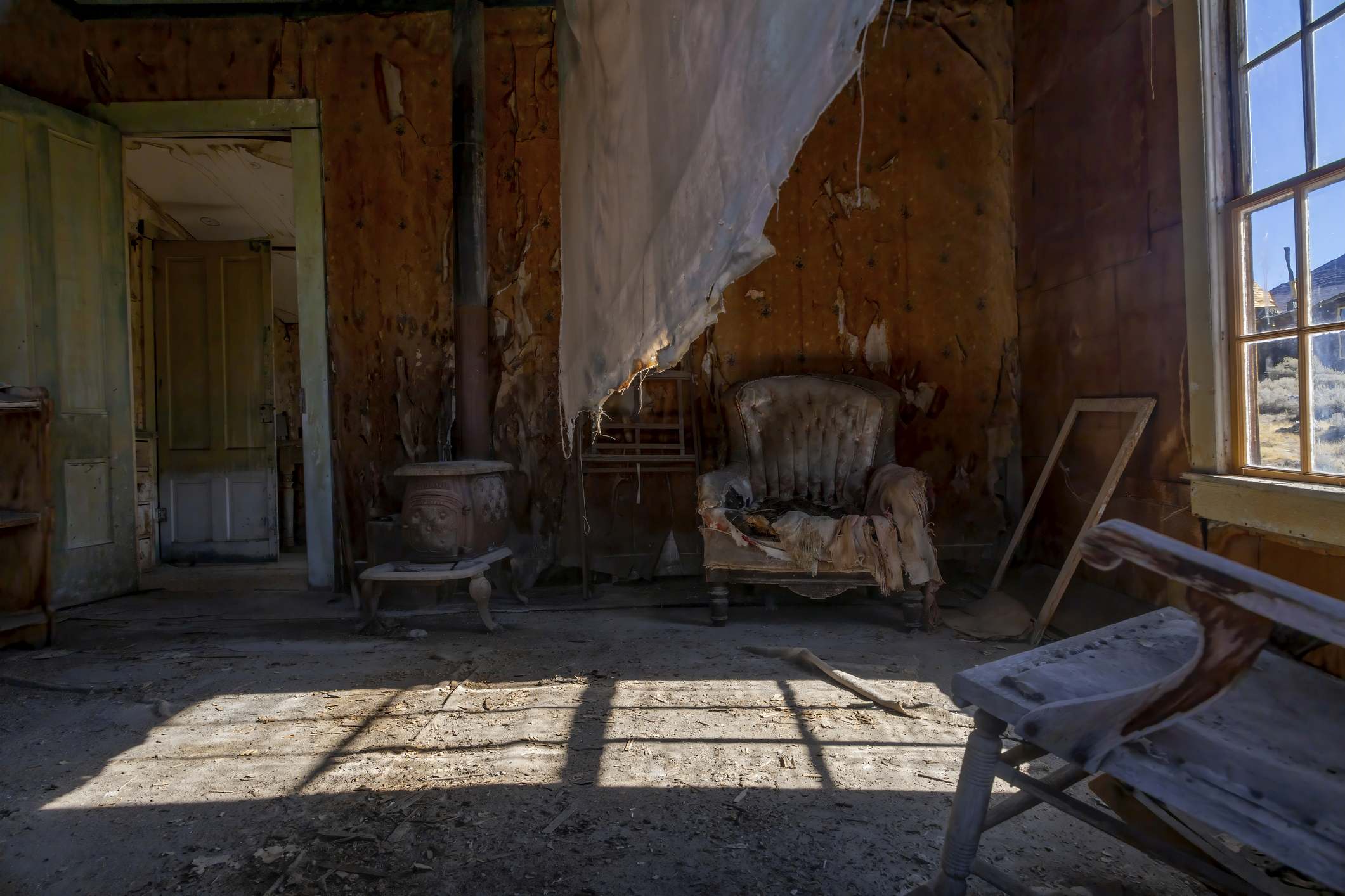 Abandoned Living Room in Bodie Ghost Town An eerie abandoned living room in Bodie, California's ghost town. Sunlight streams through broken windows, revealing decaying furniture and relics from a time long gone.