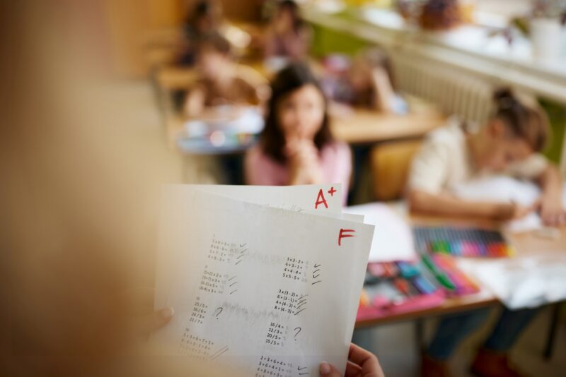 Picture Writing Prompts: Two Grades Close up of unrecognizable elementary teacher holding positive and negative test results in the classroom.