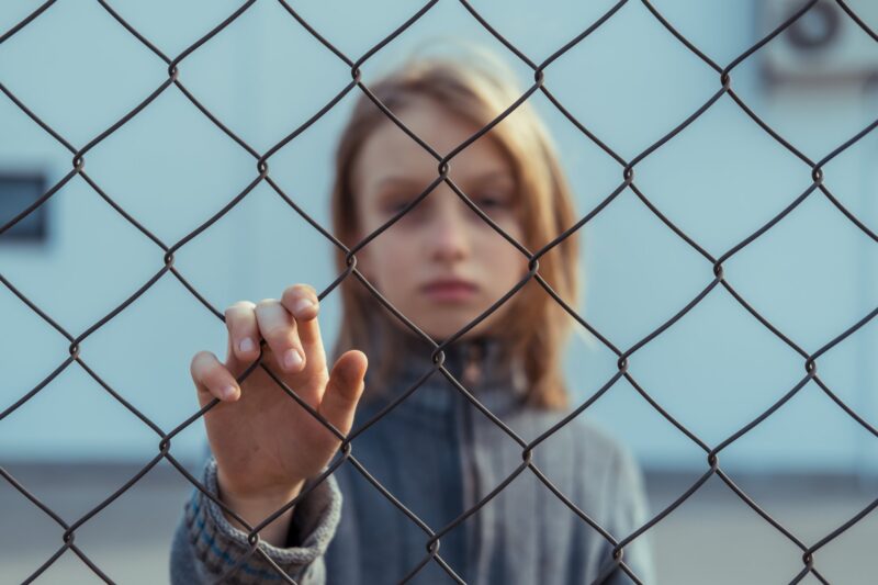 Picture Prompt: Fences Sad girl standing behind a wire fence