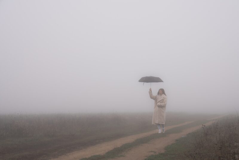 Picture Writing Prompts: Girl With Umbrella Young girl in wite coat stands in fog among the meadow on a dirt road and holds umbrella in her hand, autumn time
