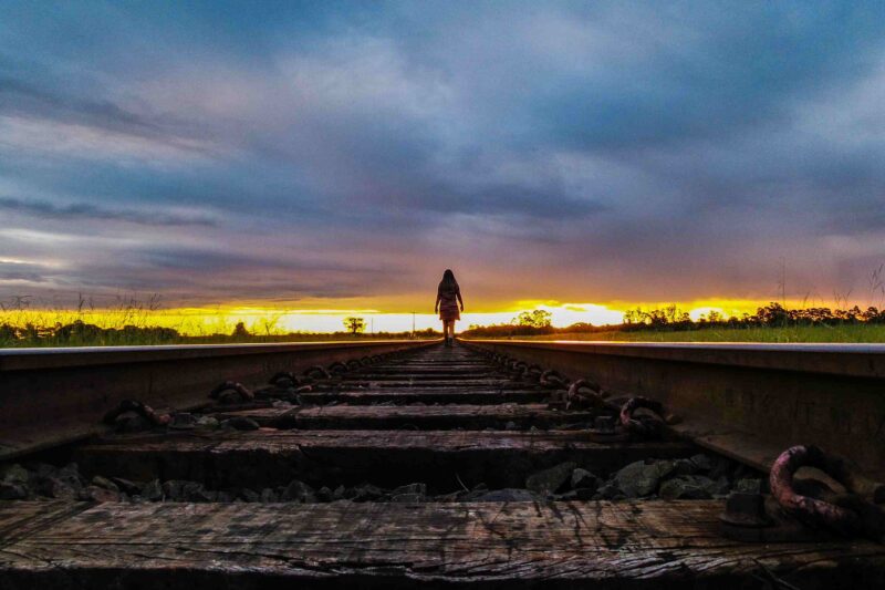 Picture Prompts: Tracks Rear View Of Woman Walking On Railroad Track Against Sky