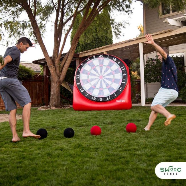 Carnival Games: Kick Darts Two men kicking rubber balls at a large inflatable dart board
