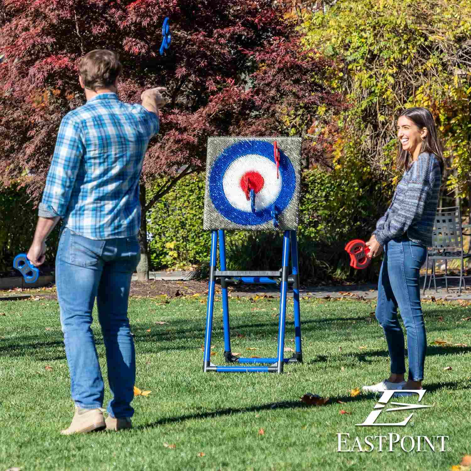 Carnival Games: Axe Throw Two people throwing toy axes at a bristle-covered target on a blue metal frame
