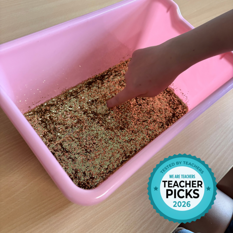 School Specialty School Smart – Glitter Student using finger to write name in a tub of glitter.